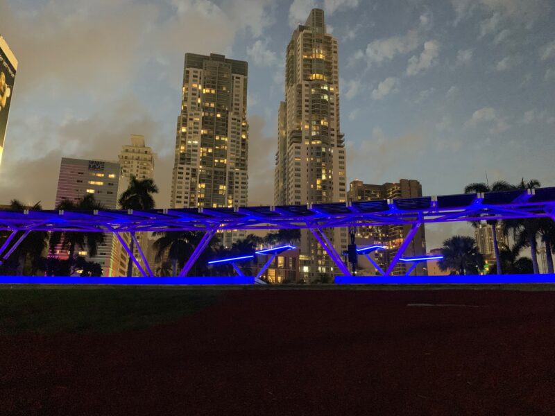 LSX Curved SolarScape lit in colored lights with solar trees at Miami Bayfront Park at Night with view of Miami in the background.
