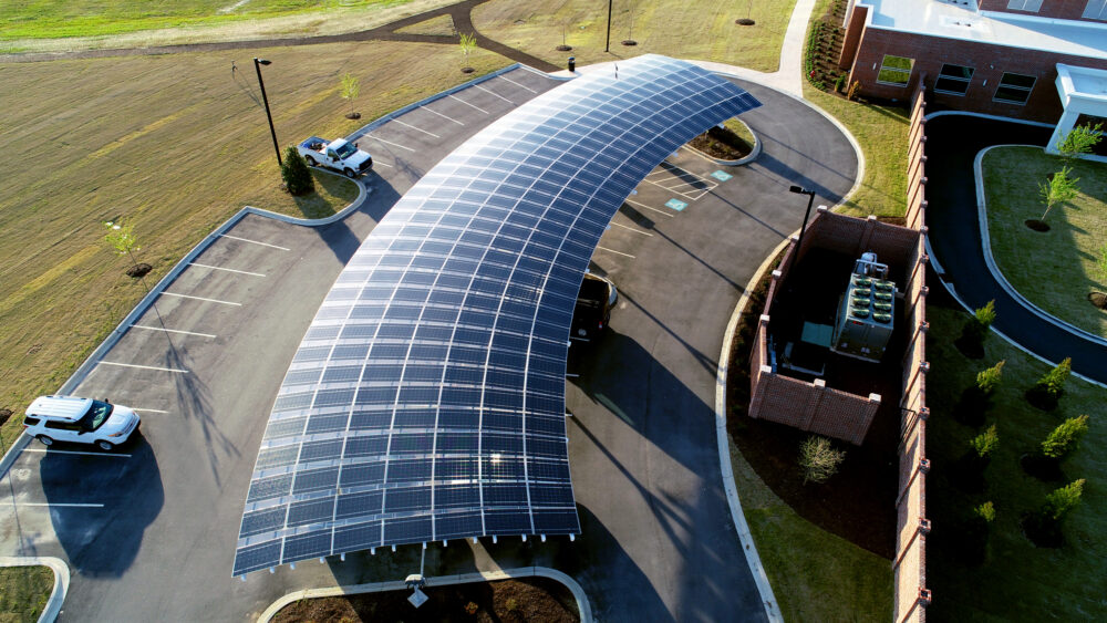 Aerial View of Solar Carport with Custom LSX Solar panels built over parking lot surrounded by grass with two cars parked at Marlboro Electric in South Carolina