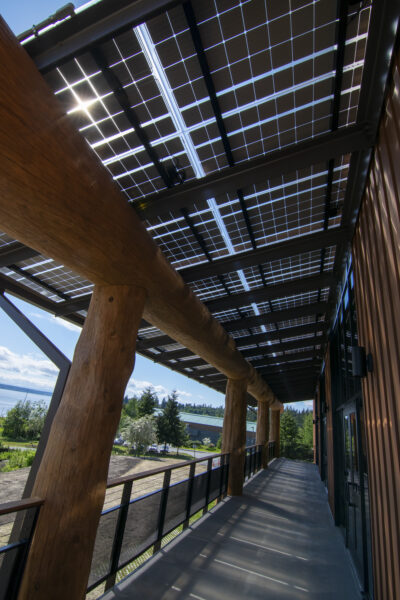 LSX Solar Panel Awning covering wraparound deck outside of Tulalip Gathering Hall with large wooden beams and view of lake in background