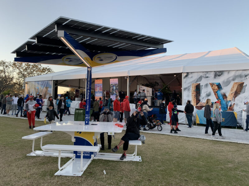 Solar Recharge Station on lawn in front of Super Bowl LV Experience with people sitting and walking by.