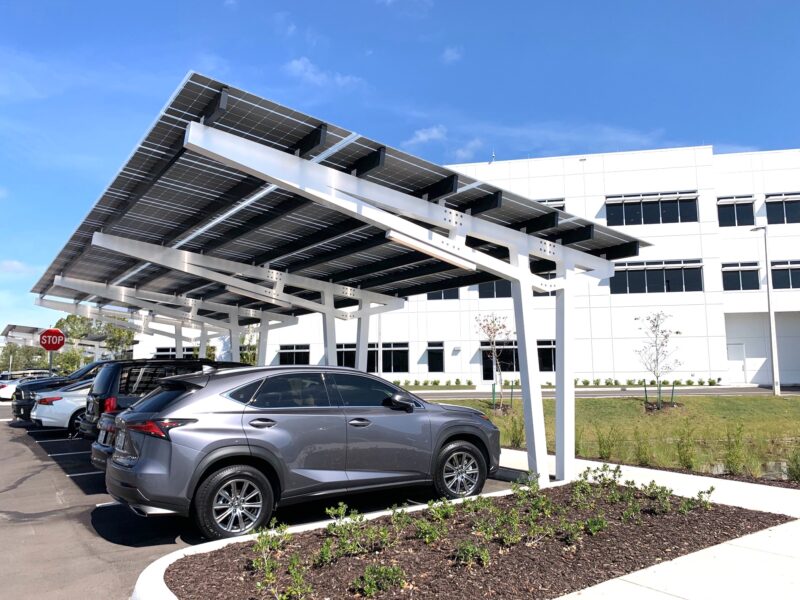 SolarScape Solar Carport with sideview of solar panels, covering parking spaces with cars parked in front of white office building