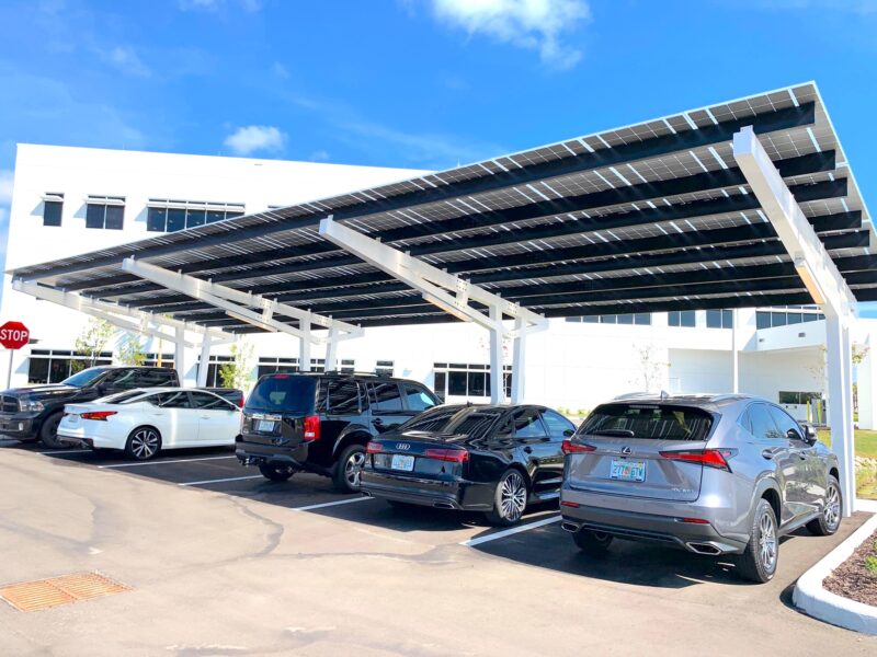 SolarScape Solar Carport with view of underside of solar panels, covering parking spaces with cars parked in front of white office building