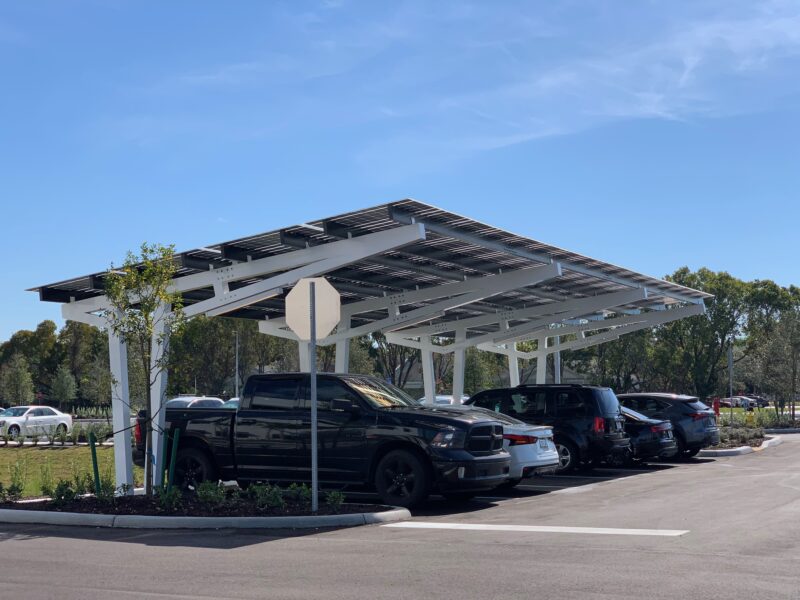 SolarScape Solar Carport covering parking spaces with cars parked and trees in background with blue sky above