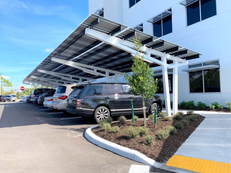 SolarScape Solar Carport covering parking spaces with cars parked in front of white office building