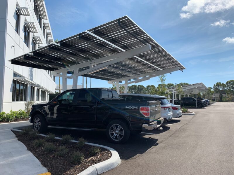 SolarScape Solar Carport covering parking spaces with cars parked and office building in background.