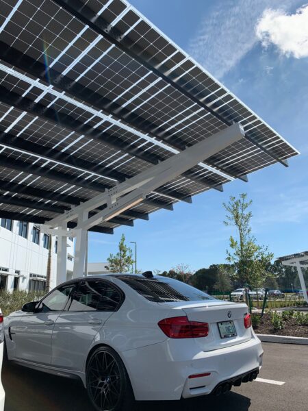 SolarScape Solar Carport covering parking spaces with car parked and office building in background.