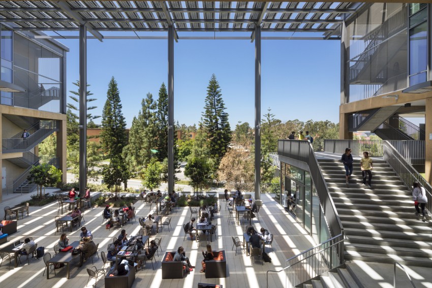 Solar Panel Awning over outdoor student area with large structural beams and tables with students sitting and studying with trees in the background