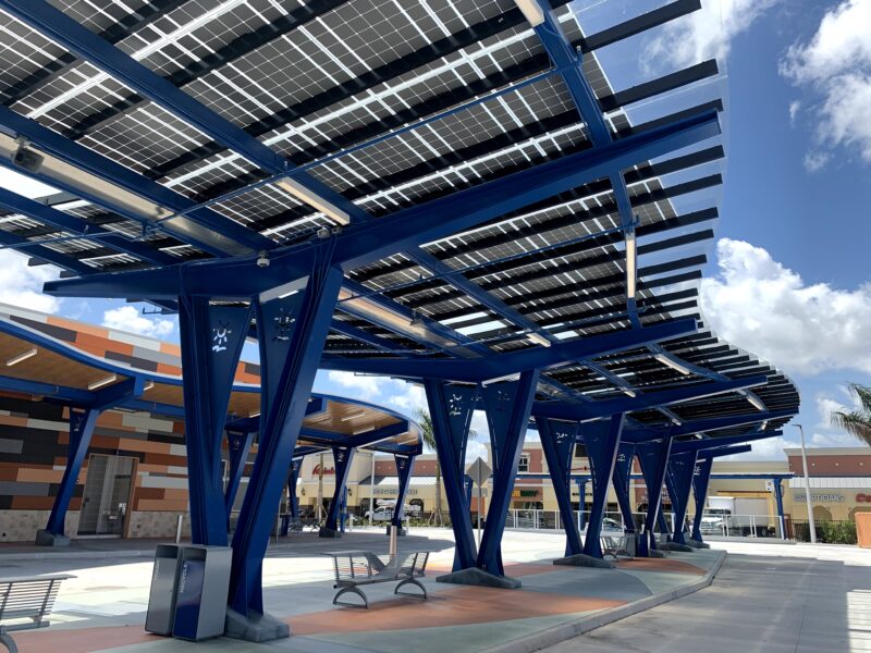 LSX Solar Canopy underside view showcases the curved design, custom blue rail system and clear frameless solar panels on the train platform at the West Lauderhill Mall Transit Center.