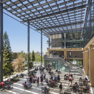 Solar Panel Awning over outdoor student area with large structural beams and tables with students sitting, studying walking around with trees in the background