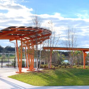LSX Curved Canopy structures providing shade and solar power on sidewalk in front of lake next to a grass lawn.